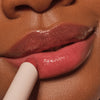 Nahaufnahme einer Person, die den Catrice Cosmetics Diamond Glaze Gloss Stick in glänzendem Pink auf ihre Lippen aufträgt.