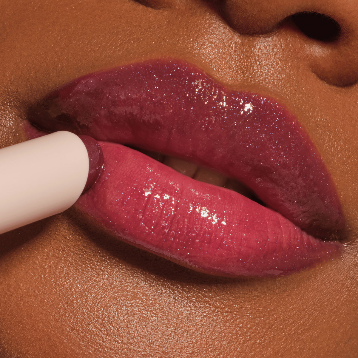 Nahaufnahme von Lippen, die mit einem beerigen, glitzernden Gloss betont werden. Der Stift wird gerade aufgetragen und verleiht intensiven Schimmer.