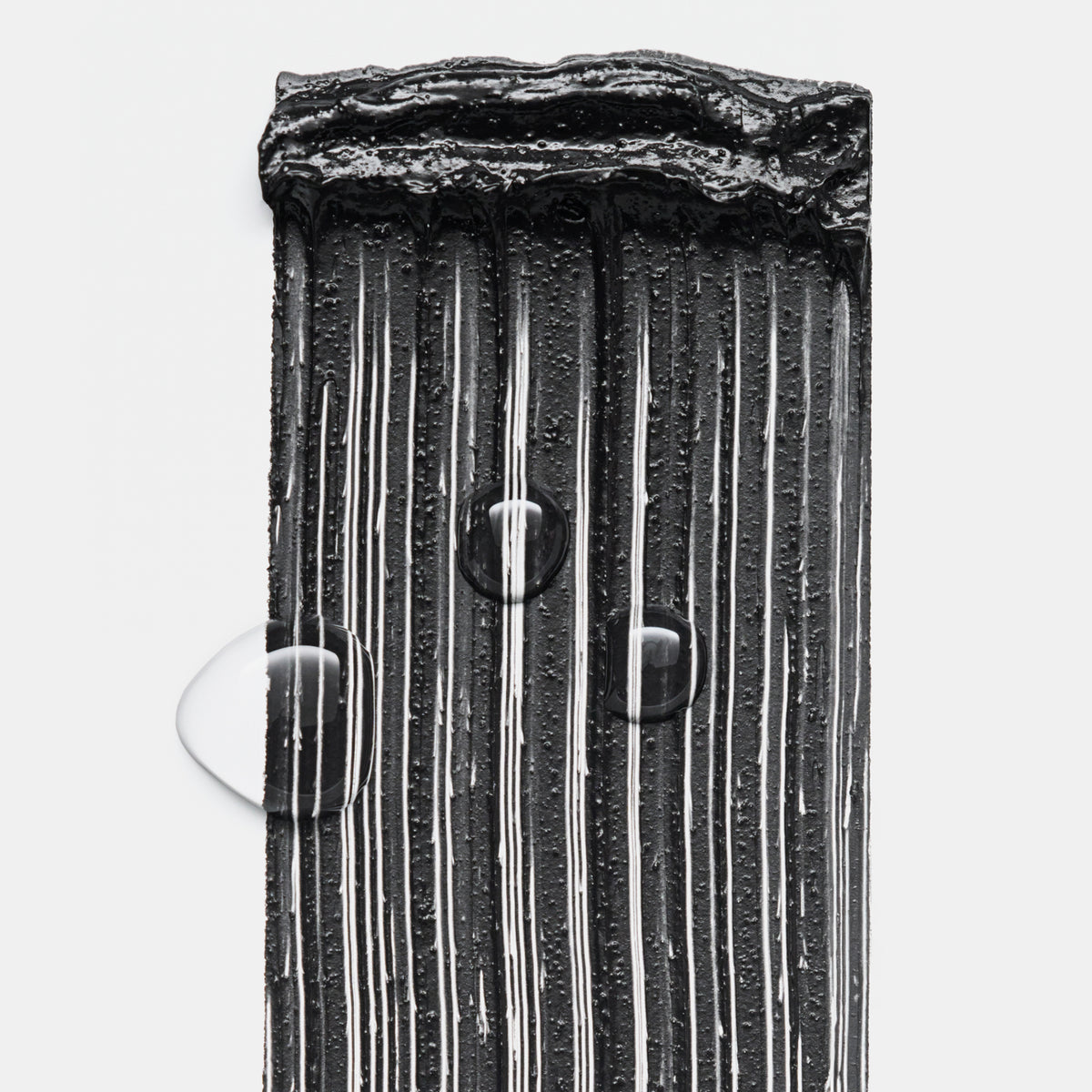 Schwarze Mascara in gleichmäßigen Streifen aufgetragen, mit sichtbaren Wasserperlen darauf, die die wasserfeste Textur zeigen.