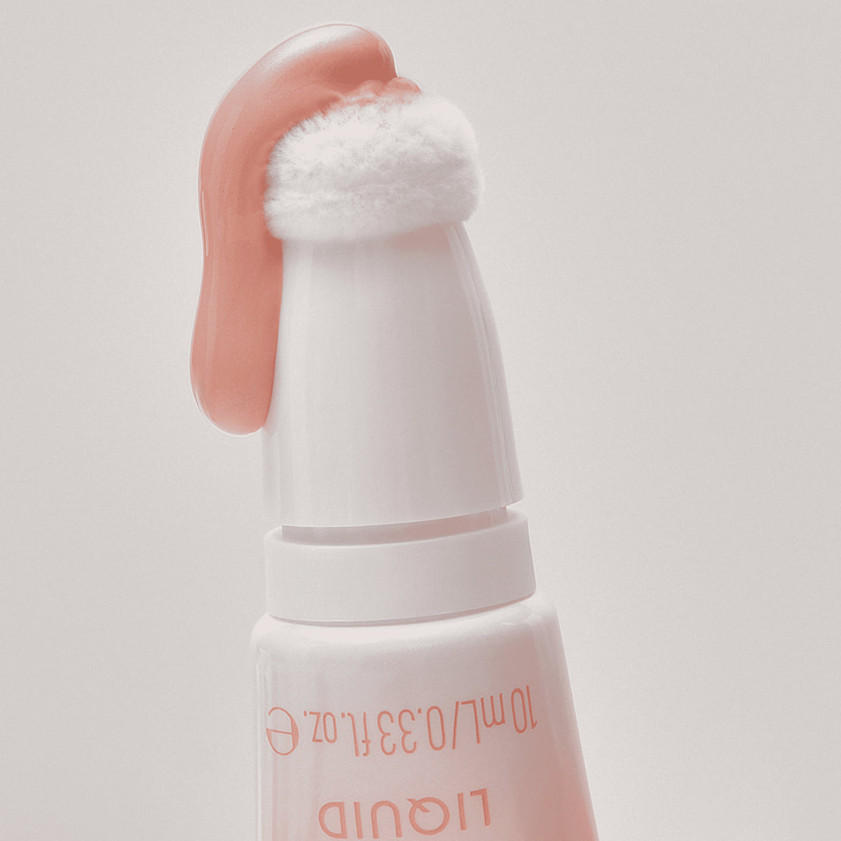 Nahaufnahme des Under Eye Brightener Liquid mit einer flauschigen Applikatorspitze und pfirsichfarbener Flüssigkeit auf der Oberseite.