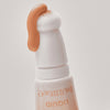 Nahaufnahme des Under Eye Brightener Liquid mit Schwammapplikator mit einer beigen Flüssigfoundation auf der Oberseite.