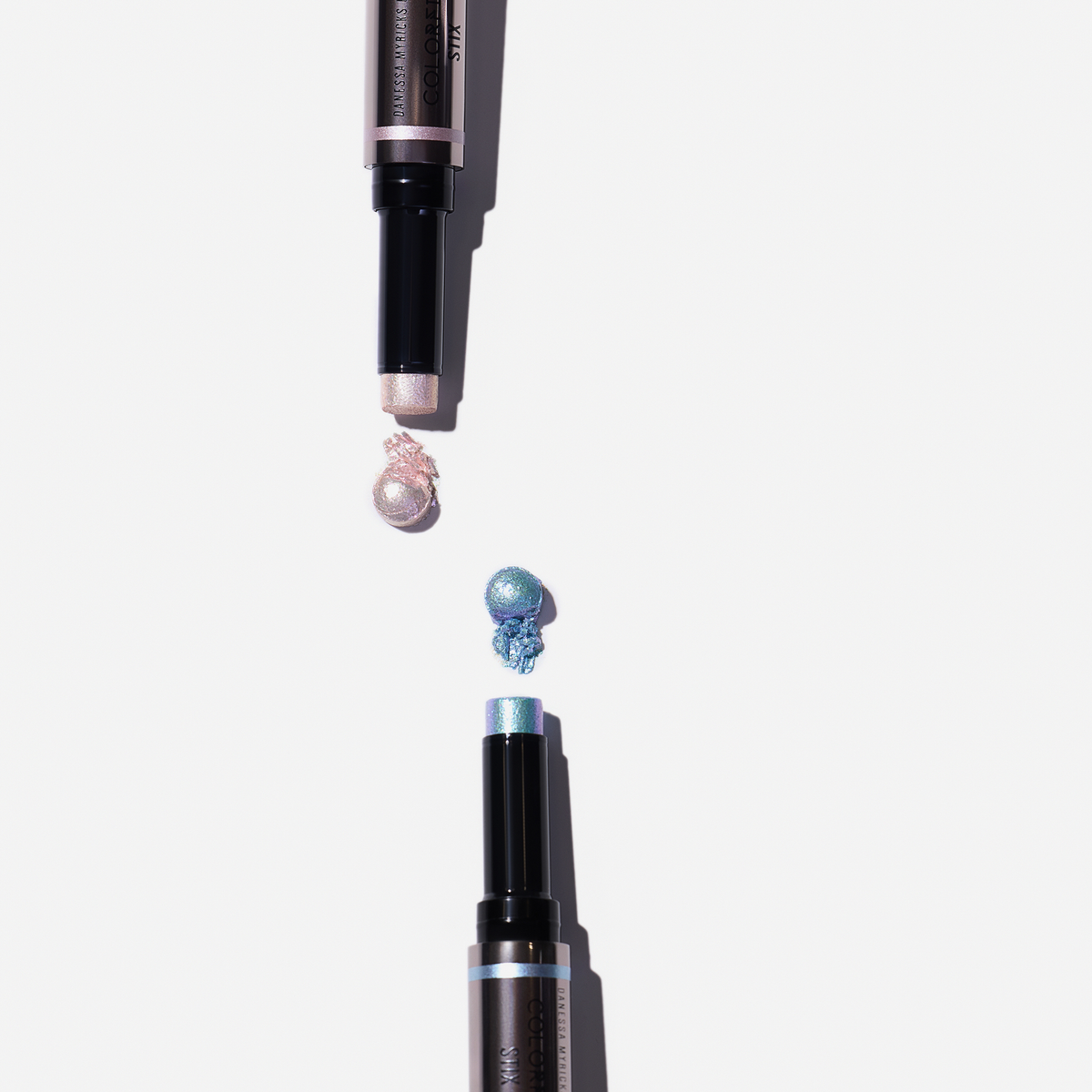 Zwei Danessa Myricks Beauty Colorfix Stix Infinity in schimmerndem Rosa und Blau auf weißem Hintergrund.