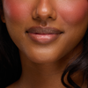 Nahaufnahme einer lächelnden Person mit glatter Haut, rosa Rouge und natürlichen Lippen, die Juicy Lip Balm von Dominique Cosmetics trägt.