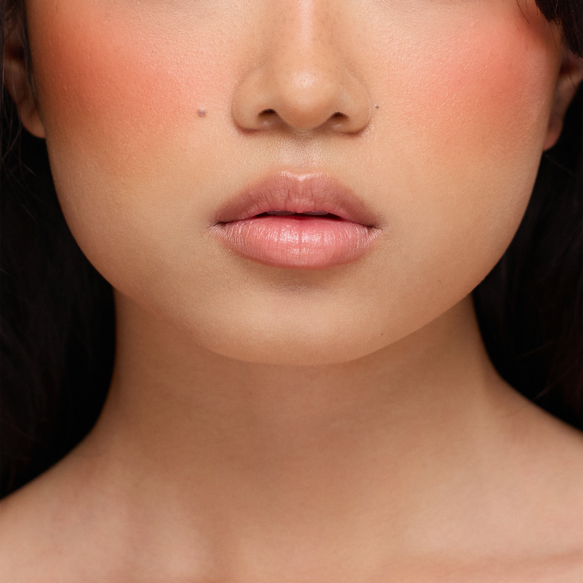 Nahaufnahme des unteren Gesichts einer Frau mit glatter Haut und natürlichem Make-up, die Dominique Cosmetics Juicy Lip Balm in einem neutralen Farbton trägt.