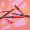 Essence 8h matte Comfort Lipliner in Rot- und Rosatönen, ohne Kappe und auf einem geometrischen Hintergrund in Rosa und Orange.