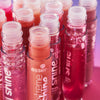 Mehrere geöffnete essence Extreme Shine Lipglosse in verschiedenen Farben stehen dicht aneinander, glänzende Texturen leuchten im Licht.