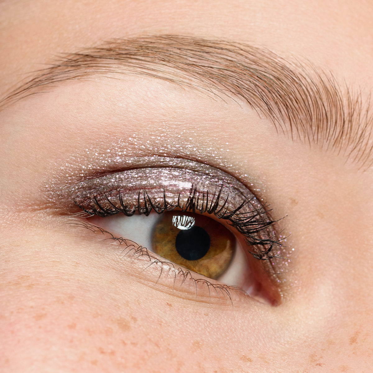 Nahaufnahme eines braunen Auges mit Essence JELLY JEWELS Glitter Stick in schimmerndem Silber, gepaart mit langen Wimpern.