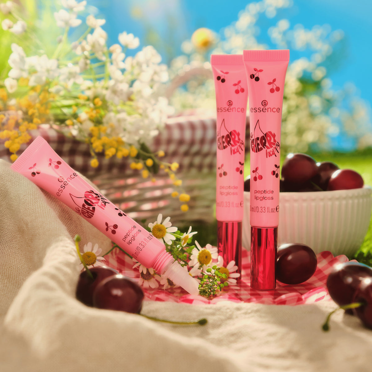 Drei SO CHERRY Happy Peptide Lipgloss-Tuben in Pink, mit Kirschen, Blumen und einer Schale Kirschen im Hintergrund.