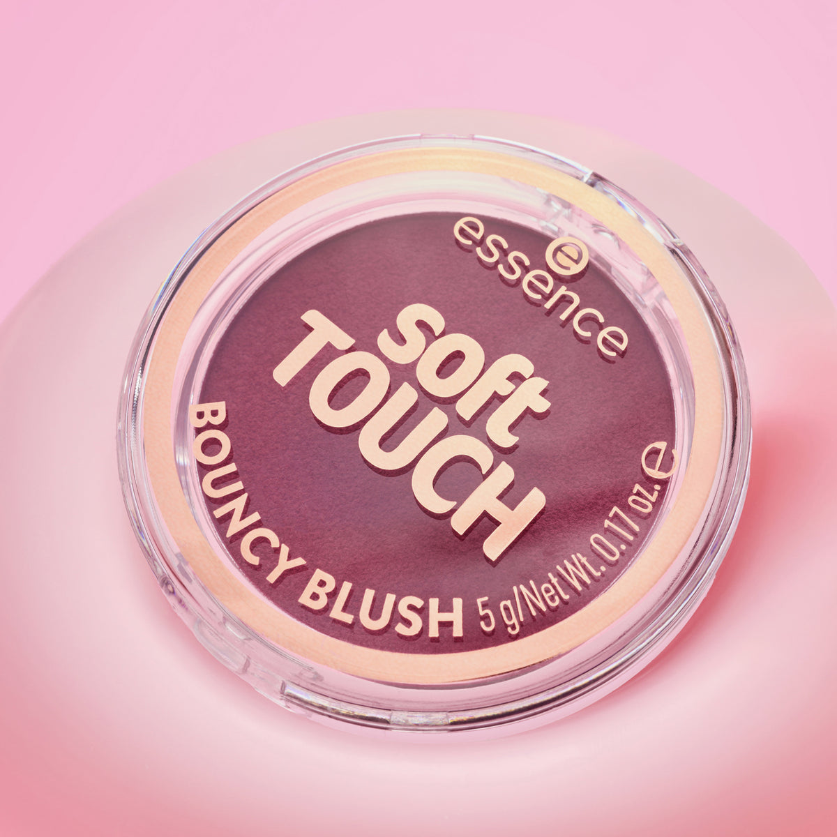 Ein runder Behälter von Essence soft TOUCH BOUNCY BLUSH ist vor einem rosa Hintergrund abgebildet.