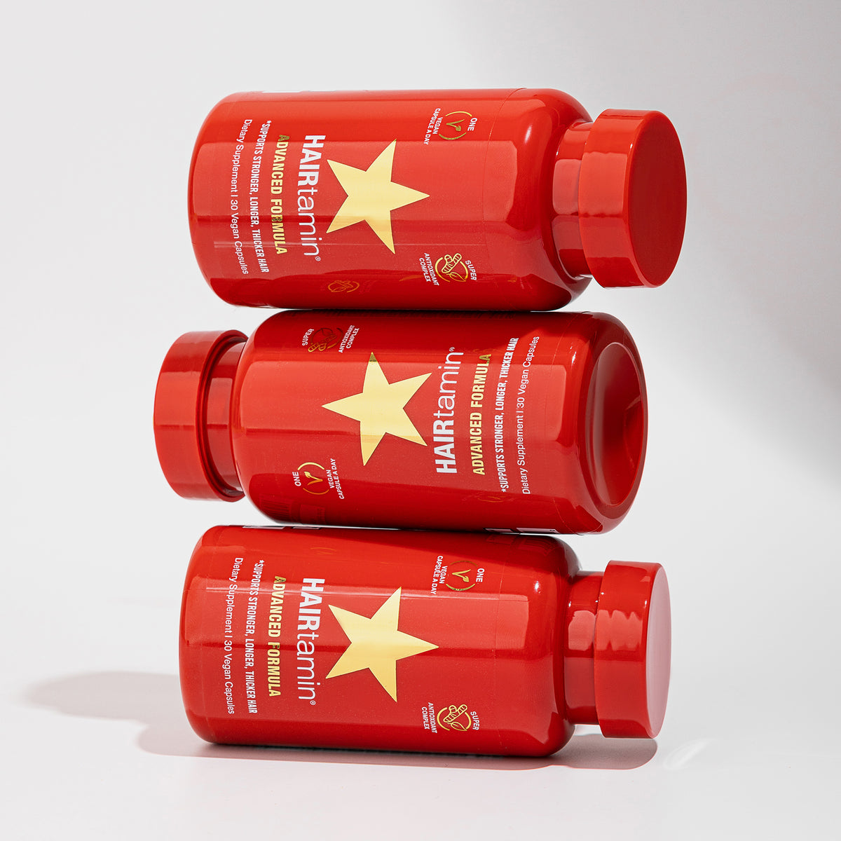 Drei horizontal gestapelte rote Advanced Formula von HAIRtamin mit goldenen Sternen auf den Etiketten vor einem weißen Hintergrund.