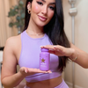 Frau in lilafarbenem Sportoutfit hält eine violette Dose BLOATAMIN Nahrungsergänzungsmittel in den Händen und lächelt in die Kamera.