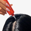 Eine Hand trägt Scalp Serum von HAIRtamin mit einer Pipette auf die Kopfhaut am Scheitel des glänzenden, schwarzen Haares auf.