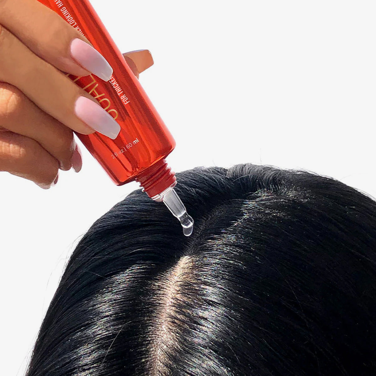 Eine Hand trägt Scalp Serum von HAIRtamin mit einer Pipette auf die Kopfhaut am Scheitel des glänzenden, schwarzen Haares auf.