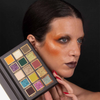 Eine Person mit auffälligem orangefarbenem Lidschatten hält die Palette „Over The Garden Wall – Tome of the Unknown“ von Lethal Cosmetics nahe an ihr Gesicht.