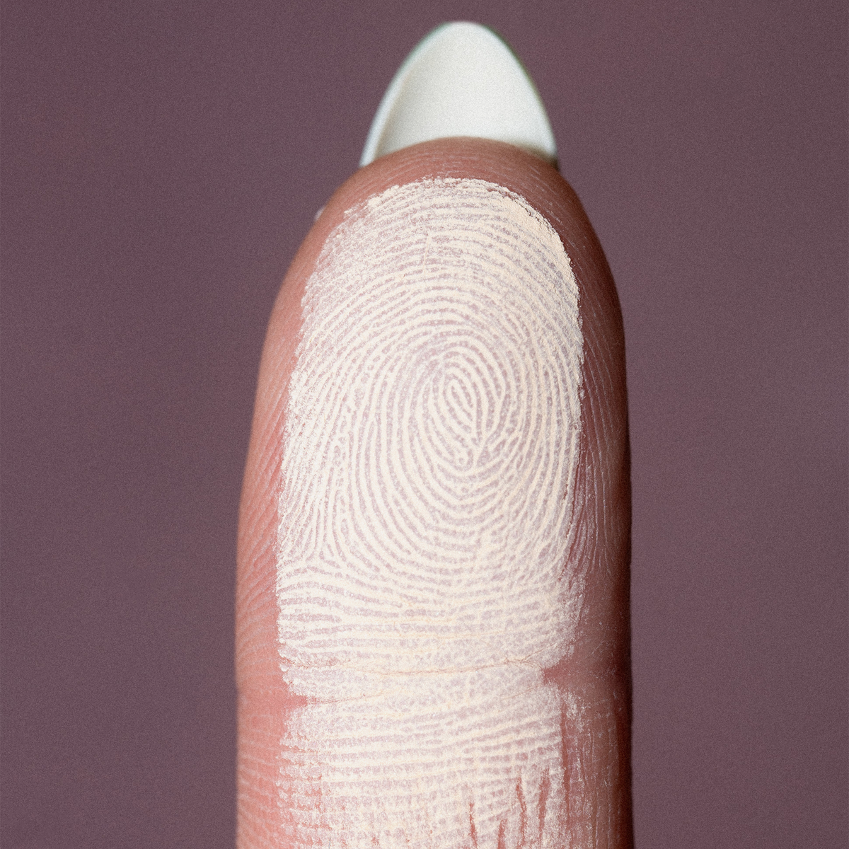Nahaufnahme einer Fingerspitze mit weißem Puder von LH Cosmetics The Single auf mauvefarbenem Hintergrund.