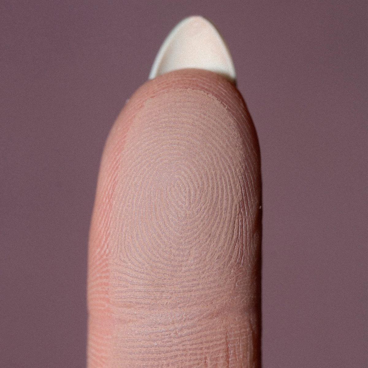Nahaufnahme einer Fingerkuppe mit einem Fingerabdruckmuster, auf dem The Single von LH Cosmetics vor einem gedämpften Hintergrund abgebildet ist.