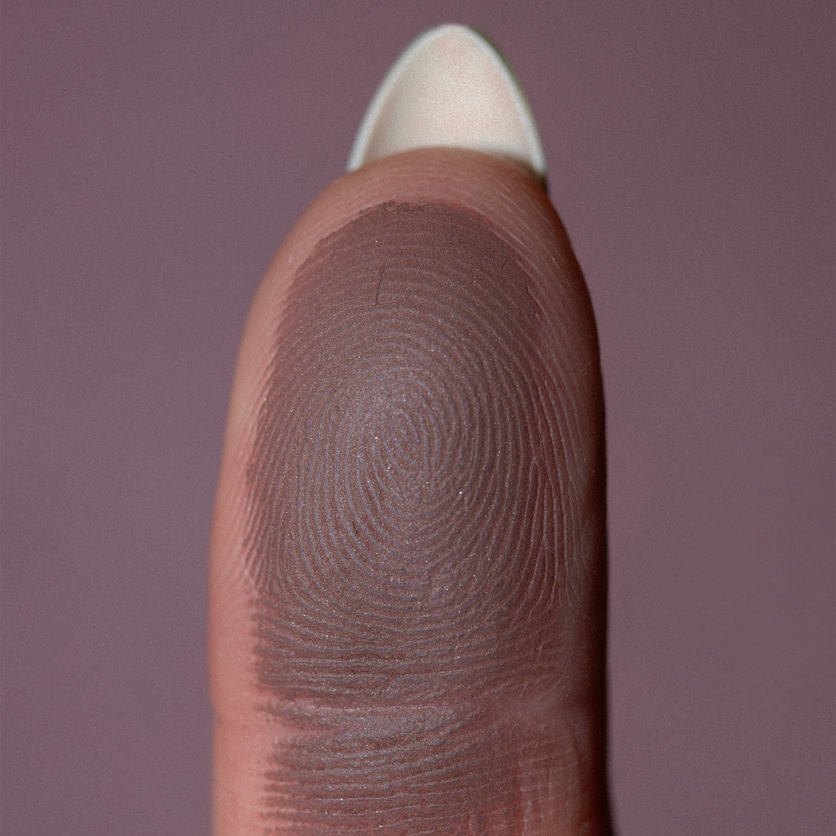 Eine Nahaufnahme einer Fingerkuppe mit detaillierten Fingerabdruckmustern zeigt The Single von LH Cosmetics vor einem unifarbenen Hintergrund.
