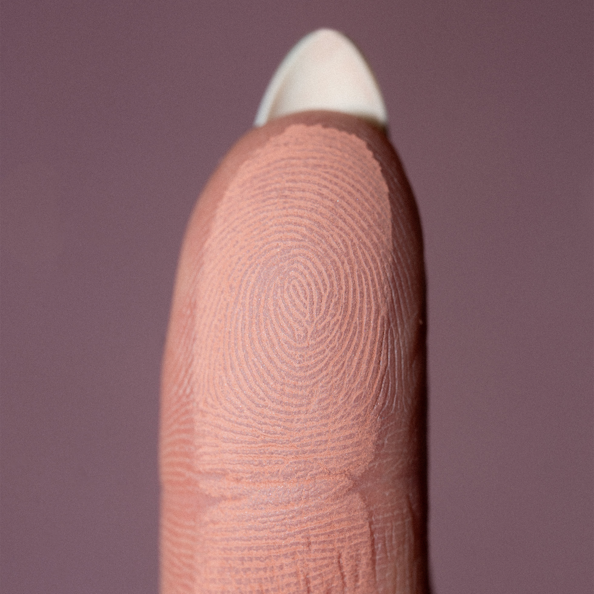 Eine Nahaufnahme einer Fingerkuppe mit detaillierten Fingerabdruckmustern, die The Single von LH Cosmetics vor einem unifarbenen Hintergrund zeigt.