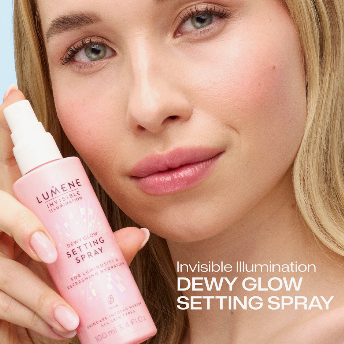 Frau mit natürlichem Glow hält Lumene Invisible Illumination Dewy Glow Setting Spray neben ihr Gesicht, Text „Dewy Glow Setting Spray“ sichtbar.