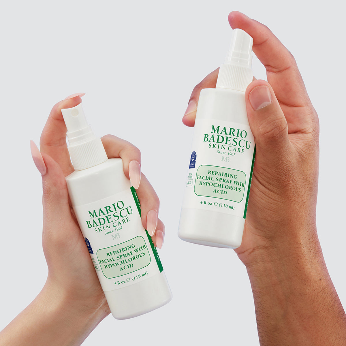 Zwei Hände halten das Repairing Facial Spray with Hypochlorous Acid von Mario Badescu vor einem hellen Hintergrund