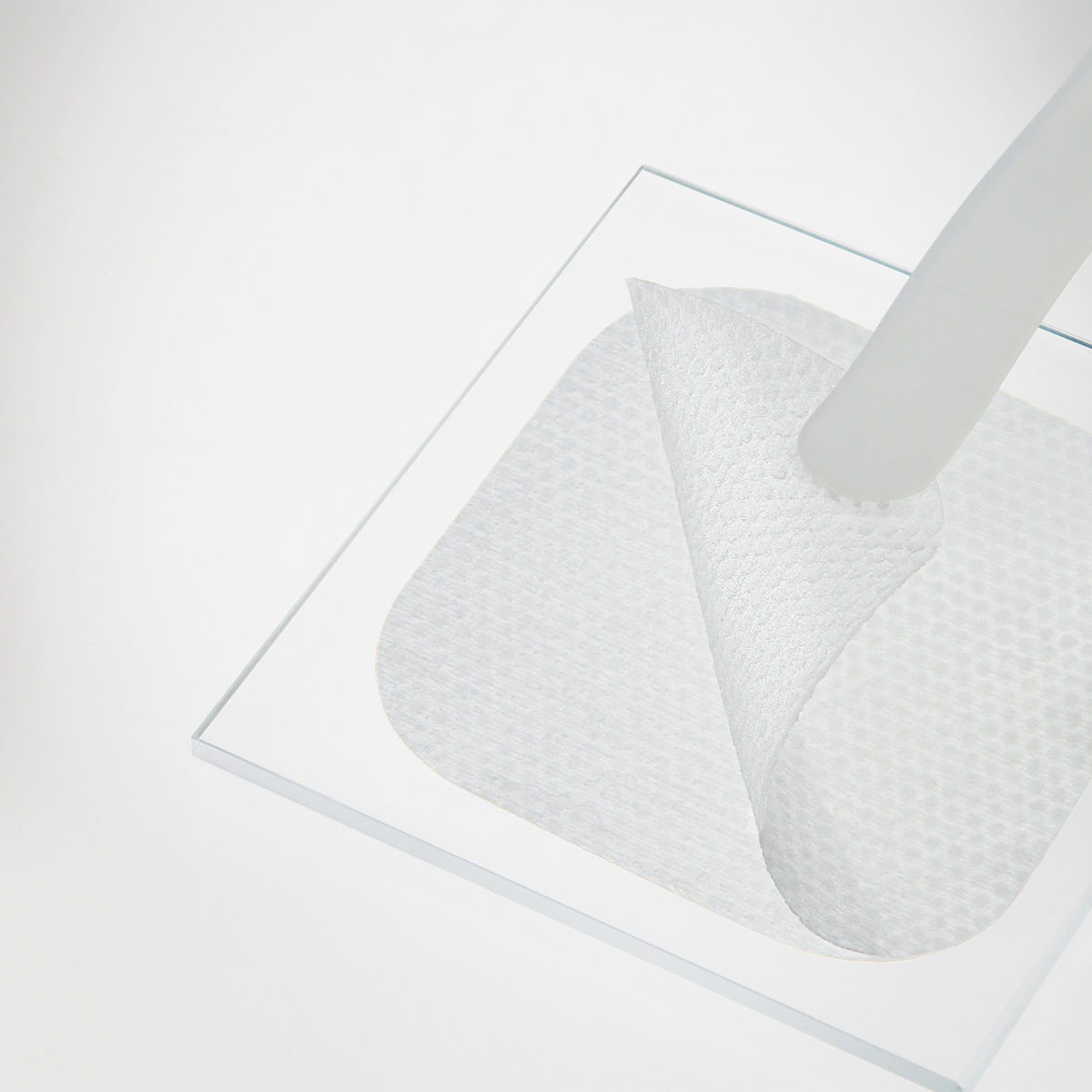 Ein „Mediheal Phyto-Enzyme Clear Peeling Pad“ wird von einer Glasoberfläche abgezogen, wodurch sein strukturiertes Muster zum Vorschein kommt.