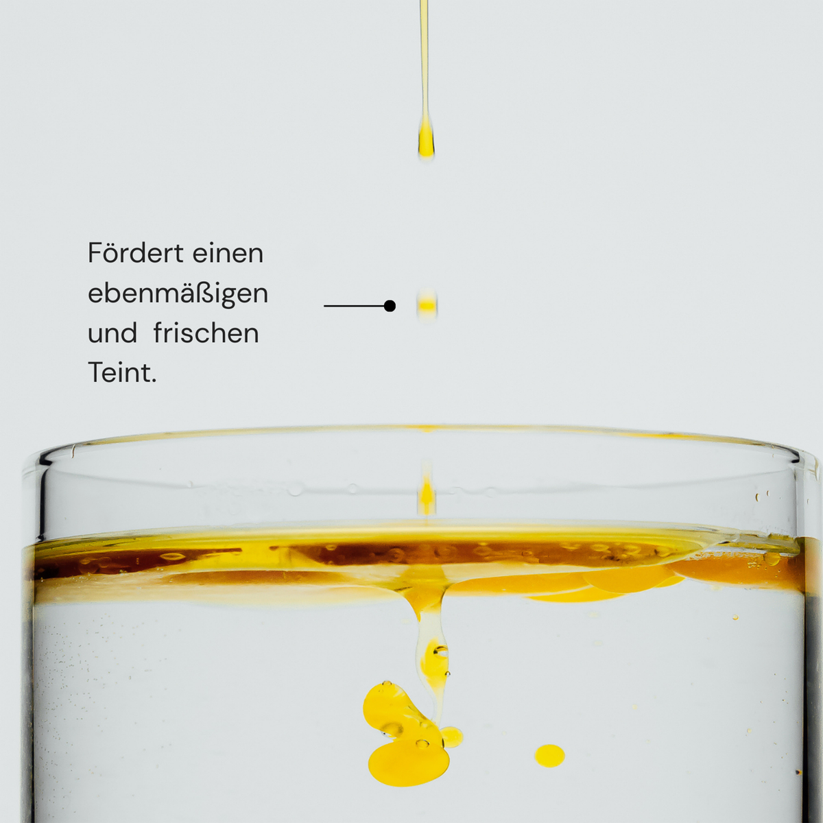 Gelbe Flüssigkeit tropft ins Wasser, mit deutschem Text: Glowing Guard Face Oil von MERME fördert einen ebenmäßigen, frischen Teint.