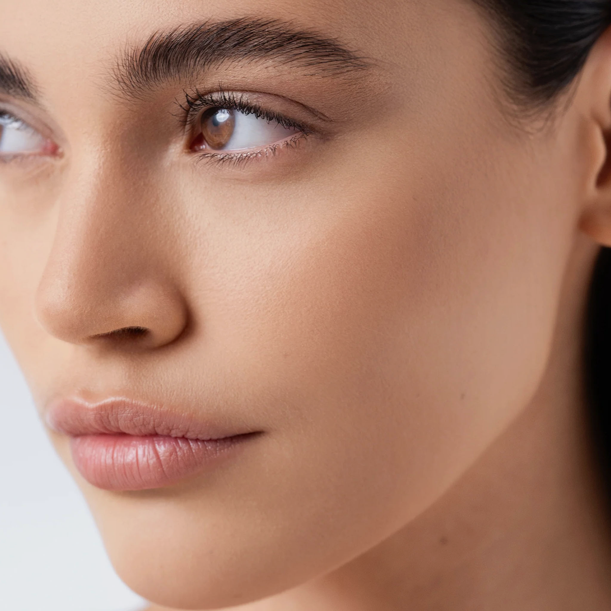 Nahaufnahme einer Frau mit klarer Haut, vollen Lippen und braunen Augen, die zur Seite schaut und Mesauda Beauty Chrono Flawless Primer trägt.