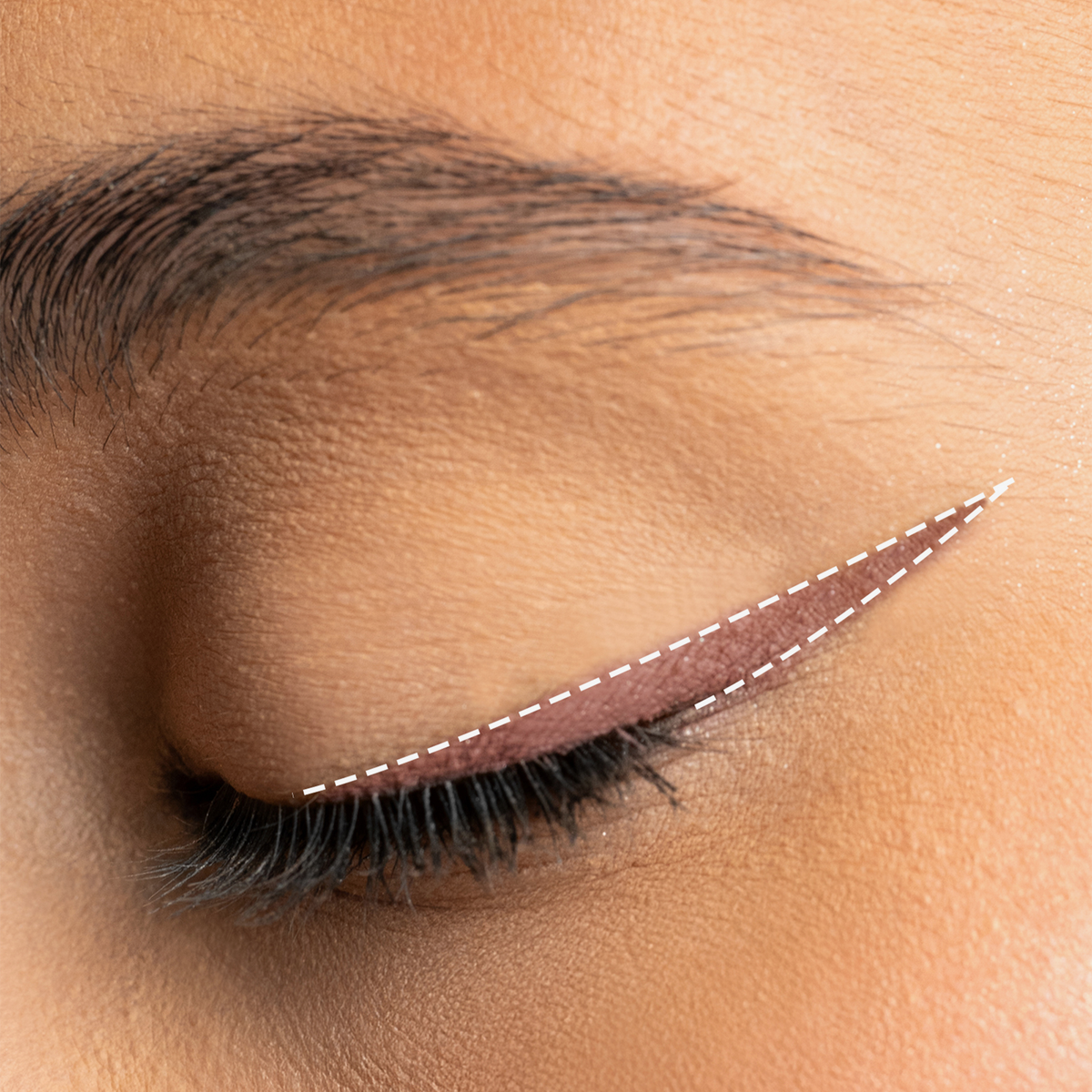 Ein geschlossenes Auge zeigt einen braunen, geflügelten Eyeliner, der mit dem Mesauda Milano Drawmatic Shadow aufgetragen wurde und durch weiße, gestrichelte Linien hervorgehoben wird, die die Form des Eyeliners konturieren.