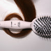 Eine Miracle Brush® X HAIRtamin® liegt auf einer braunen Haarsträhne auf weißem Hintergrund.