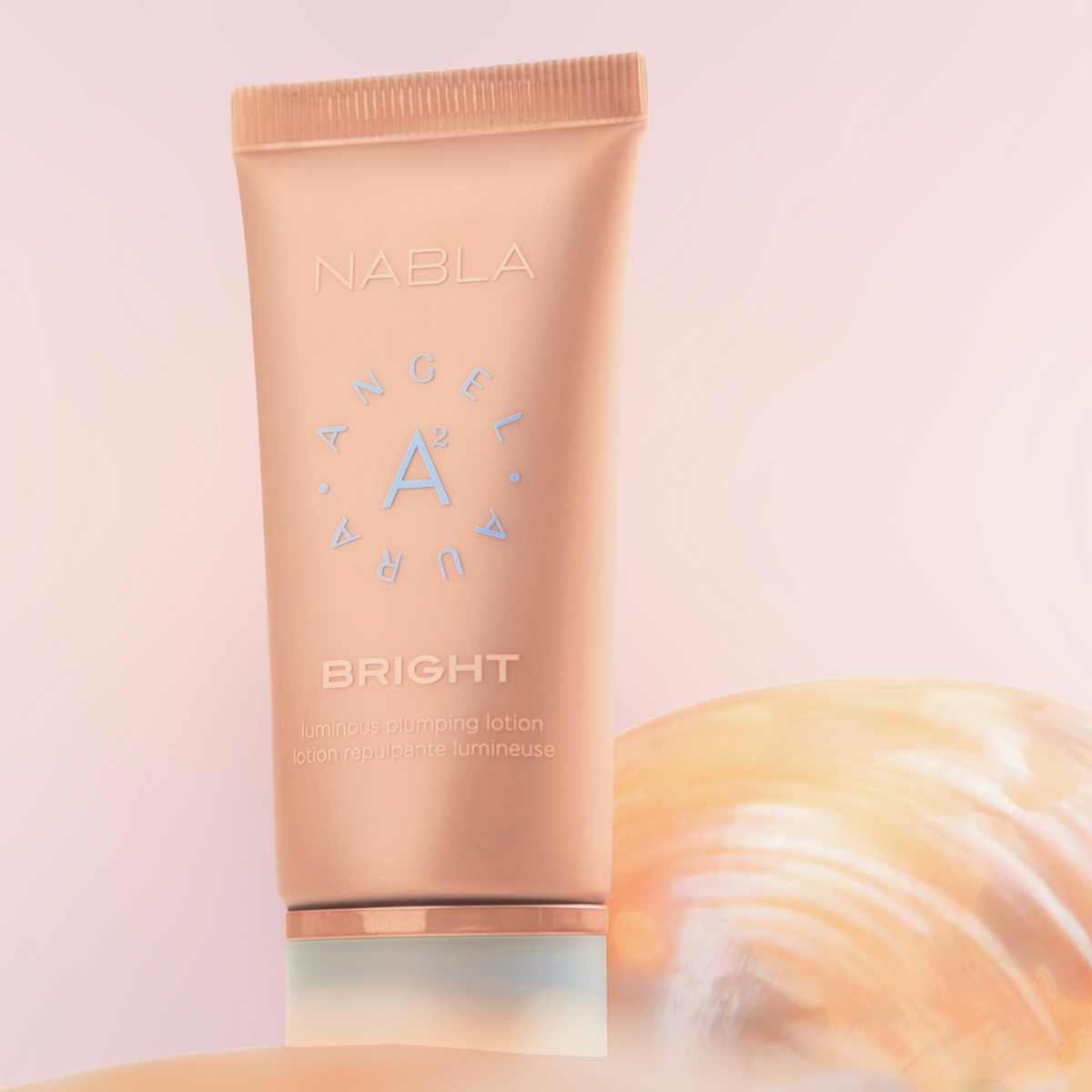 Pfirsichfarbene Tube der NABLA Cosmetics Angel Aura Bright auf zartrosa Hintergrund.