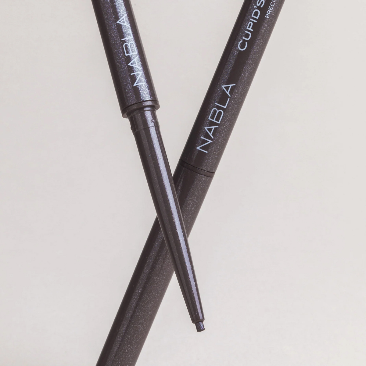 Zwei NABLA Cosmetics Cupids Arrow Micro Eyeliners in Dunkelbraun, gekreuzt, einer mit freiliegender Spitze, auf hellem Grund.