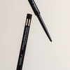 Zwei schwarze NABLA Cosmetics Cupids Arrow Micro Eyeliners: einer mit Kappe, einer mit freiliegender Spitze.
