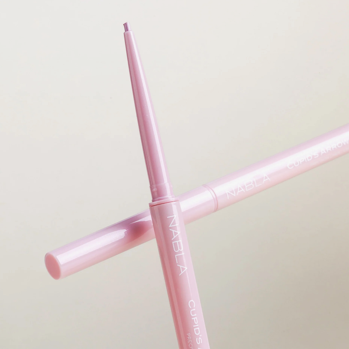 Ein rosafarbener NABLA Cosmetics Cupids Arrow Micro Bleistift mit ausgezogener Spitze, auf einem passenden geschlossenen Bleistift platziert.