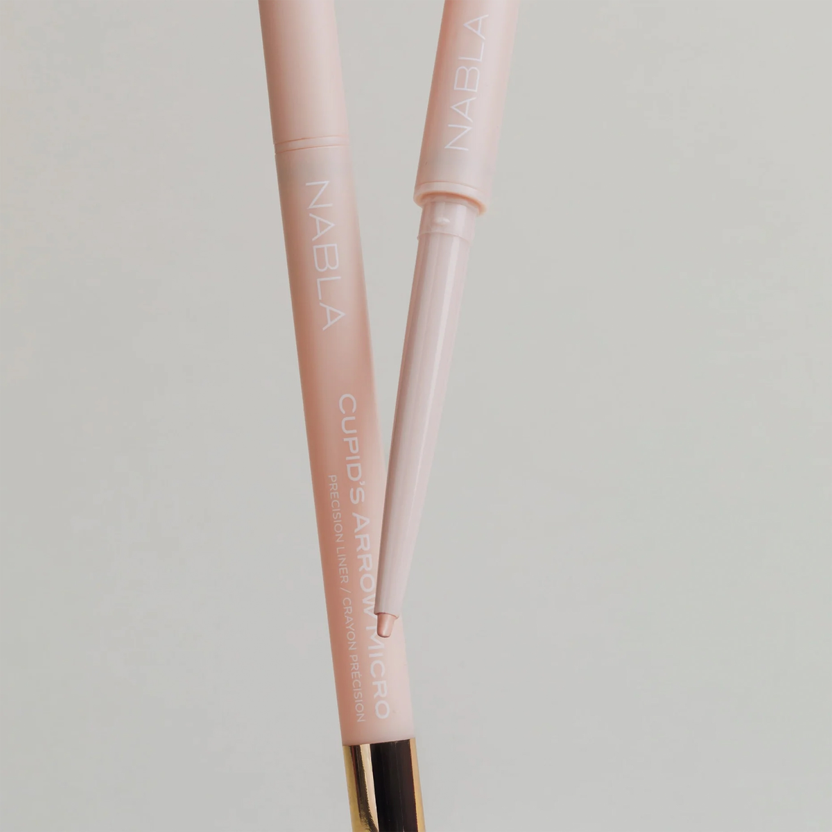 Zwei rosafarbene NABLA Cosmetics Cupids Arrow Micro Augenbrauenstifte, einer ohne Kappe, um die Präzisionsspitze zu zeigen, auf einem hellen Hintergrund.