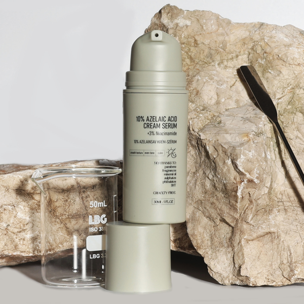 NERDS 10% Azelaic Acid Cream Serum vor Natursteinen, mit Becherglas und Spatel – minimalistisches, wissenschaftliches Produkt-Stillleben.