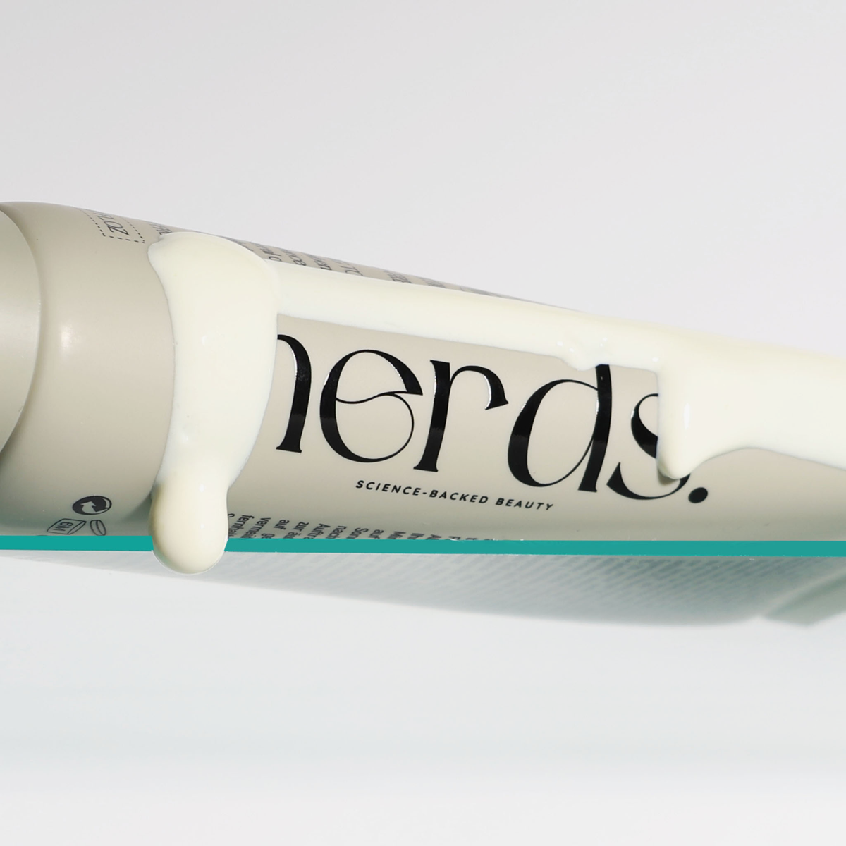 Eine Tube der NERDS. Lightweight Hydrate UV Defense Lotion SPF50 liegt auf Glasregal, Lotion auf der Tube vor einem weißen Hintergrund.