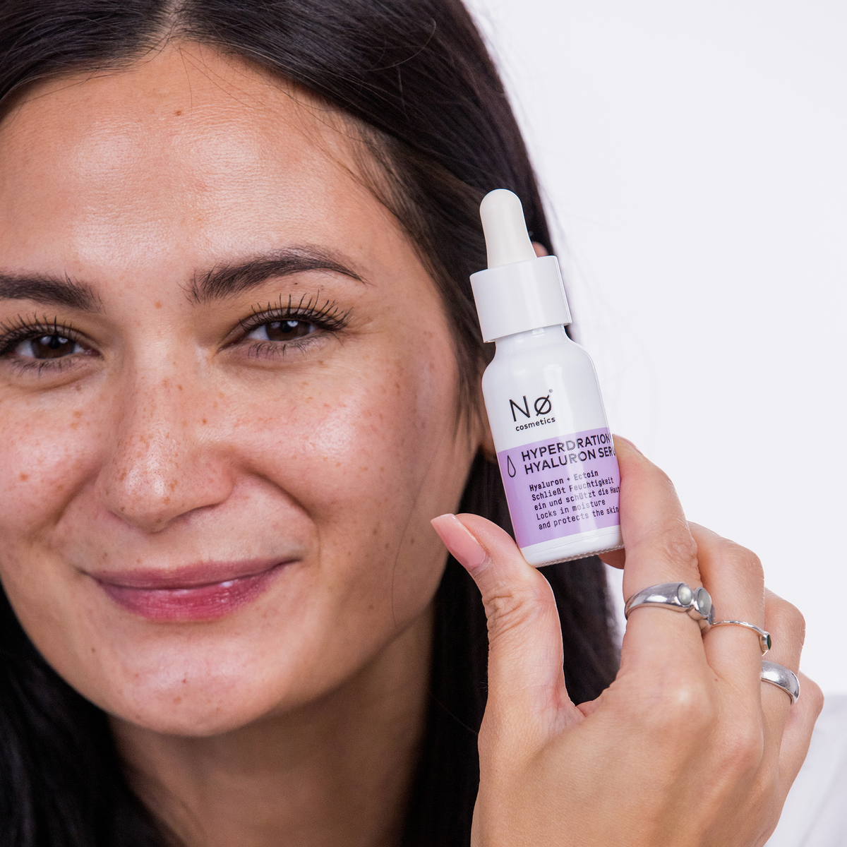 Eine lächelnde Frau hält eine Flasche Hyperdration® Hyaluron Serum von Nø Cosmetics nahe an ihr Gesicht.
