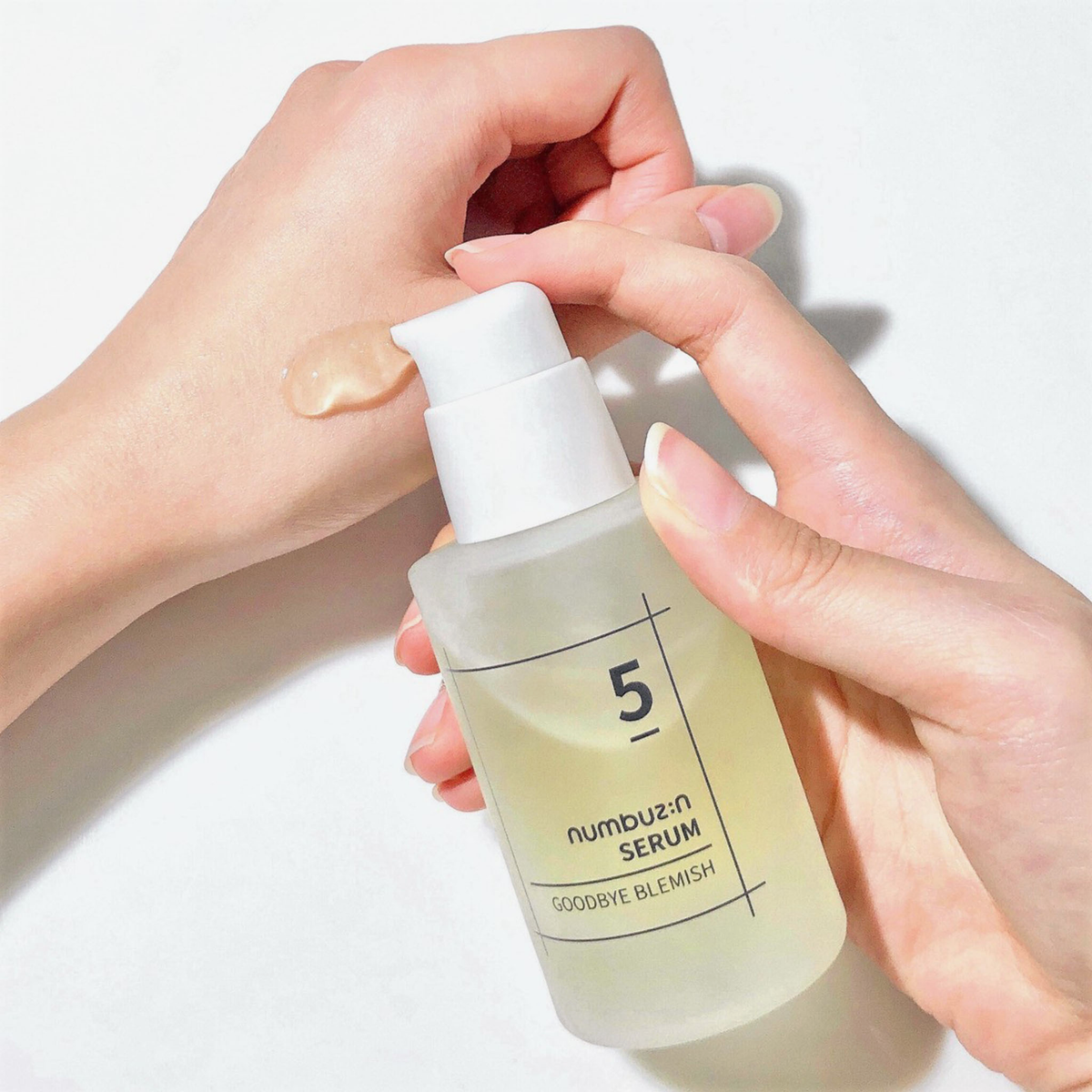 Eine Hand trägt das Numbuzin No.5 Goodbye Blemish Serum aus einer durchsichtigen Pumpflasche auf den Rücken einer anderen Hand auf.