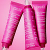 Drei Tuben des Paula's Choice Pro-Collagen Peptide Gloss Balm sind auf einem rosa Hintergrund abgebildet.