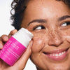 Eine lächelnde Person mit Sommersprossen hält eine Flasche Paula's Choice Pro-Collagen Peptide Plumping Feuchtigkeitscreme an ihre Wange.