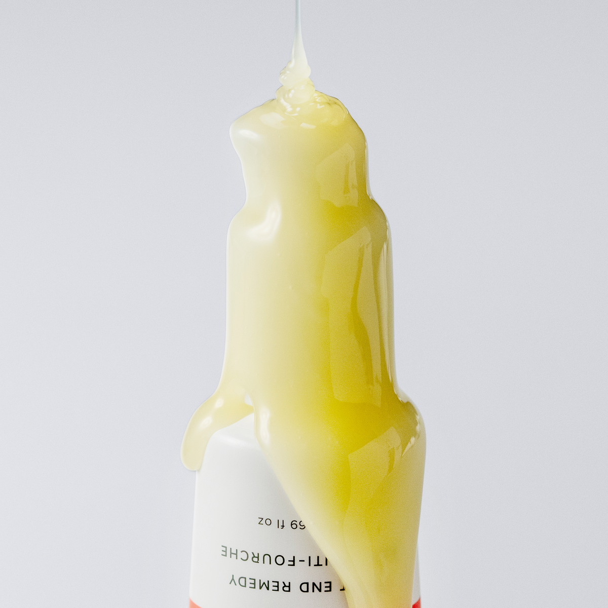 Eine gelbe Flüssigkeit tropft auf eine weiße Flasche „Philip Kingsley Bond Builder Split End Remedy“ mit schwarzer Schrift auf weißem Hintergrund.