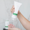 Eine Person drückt unter der Dusche etwas Philip Kingsley Flaky Itchy Scalp Conditioner in die Hand, während das Wasser über beide Hände läuft.