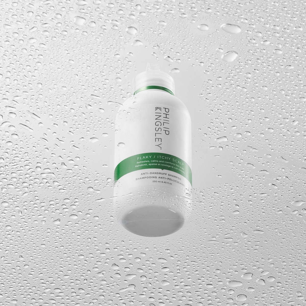 Eine weiße Flasche „Philip Kingsley Flaky Itchy Scalp Shampoo“ steht auf einer nassen, mit Wassertropfen übersäten Oberfläche, auf der sich Kondenswassertropfen gebildet haben.