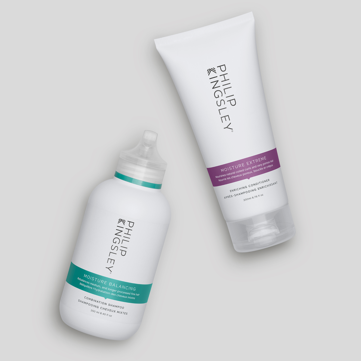 Zwei Flaschen von Philip Kingsley, darunter das „Moisture Balancing Shampoo“ und die Spülung, schräg auf einem hellgrauen Hintergrund.