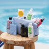 Die PURISH Summer Bag 2025 – Deluxe Routine steht auf einem Holzhocker neben einem Pool und enthält eine Reihe von Hautpflegeprodukten in einer stilvollen blauen Kulturtasche.