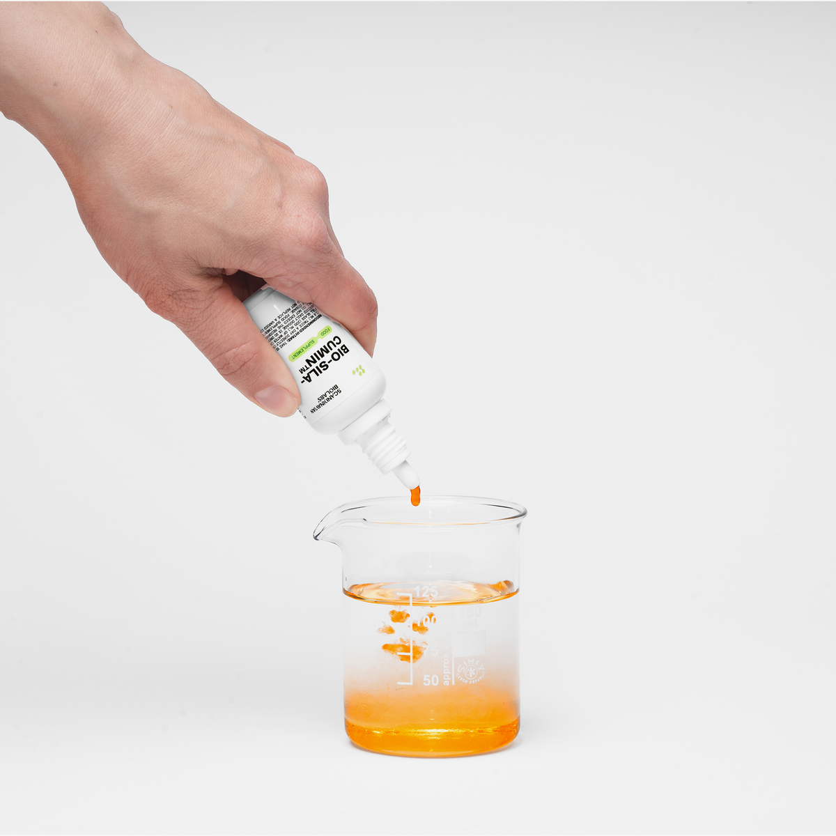 Eine Hand tropft orangenes Bio-Silacumin von Scandinavian Biolabs in ein klares Becherglas mit Wasser.