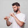 Ein Mann in einem weißen T-Shirt hält ein Glas Wasser in der Hand und bereitet sich auf die Einnahme von Scandinavian Biolabs Hair Nutrient Tablets vor.