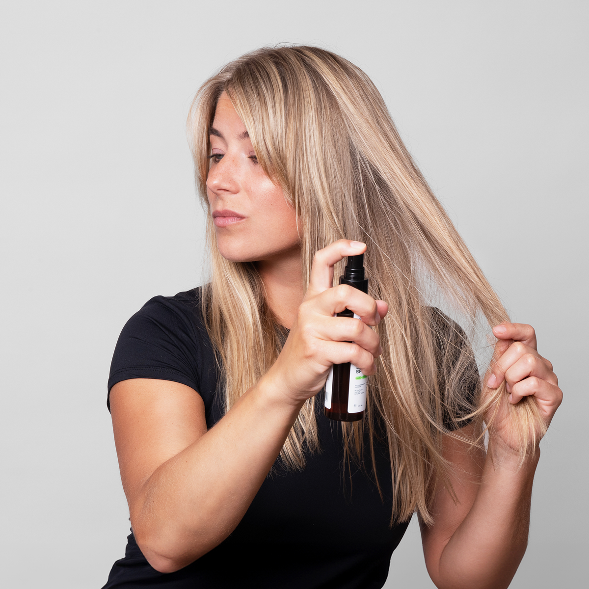 Eine Frau sprüht Scandinavian Biolabs Sea Mineral Spray auf ihr langes blondes Haar, während sie einen Teil davon mit der Hand festhält.