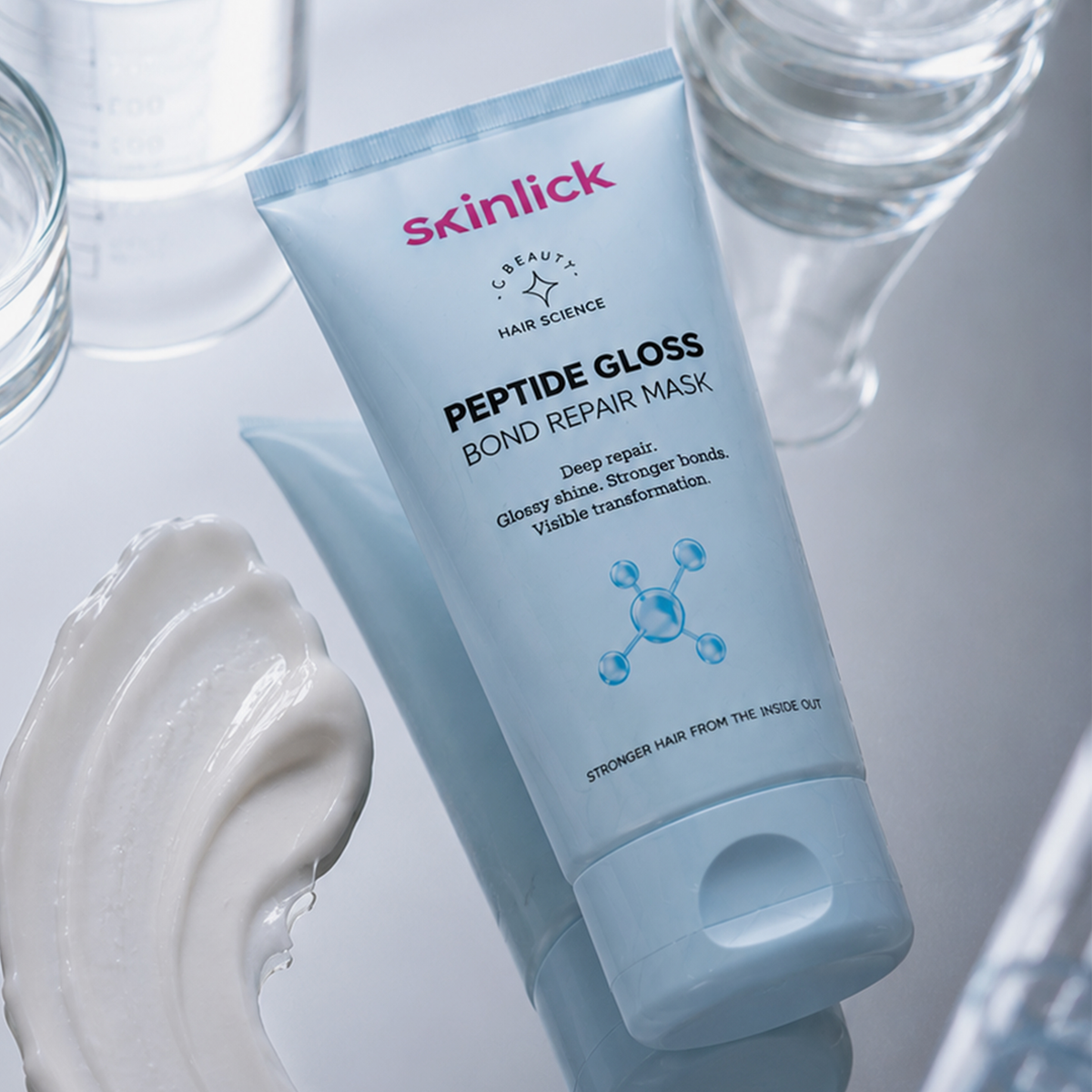 Eine Tube „skinlick Peptide Gloss Bond Repair Mask“ auf einer spiegelnden Oberfläche, daneben Wasser und cremefarbene Akzente.