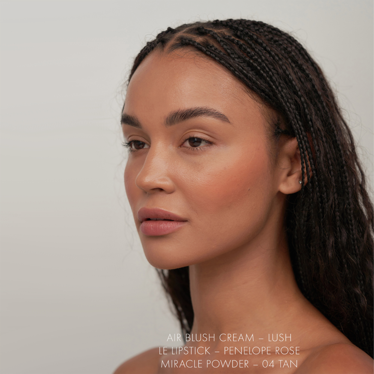 Frau mit langen Zöpfen und natürlichem Make-up, Blick nach links. Zum Make-up gehört die SWEED Air Blush Cream. Neutraler Hintergrund.